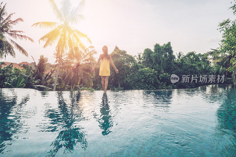 巴厘岛乌布，一名年轻女子张开双臂，站在无边泳池边