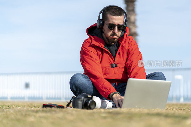 一个年轻人坐在草地上用笔记本电脑玩智能手机