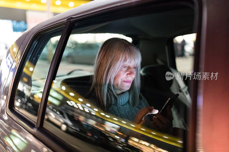 美丽成熟的女人在出租车上使用智能手机