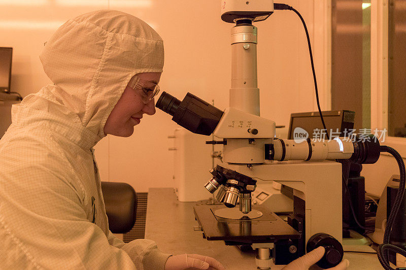 年轻女子在半导体制造环境或无尘室使用显微镜检查