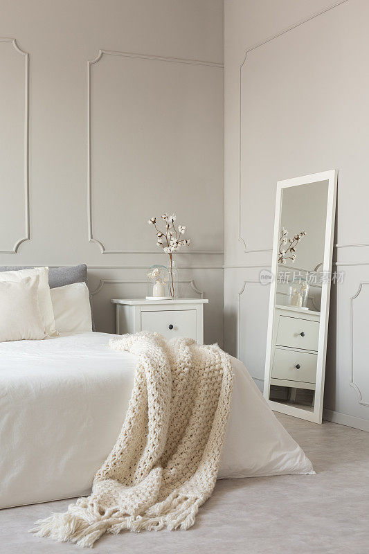 镜子在白色框架上的灰色墙壁时尚的斯堪的纳维亚卧室室内与特大号床和舒适的毯子