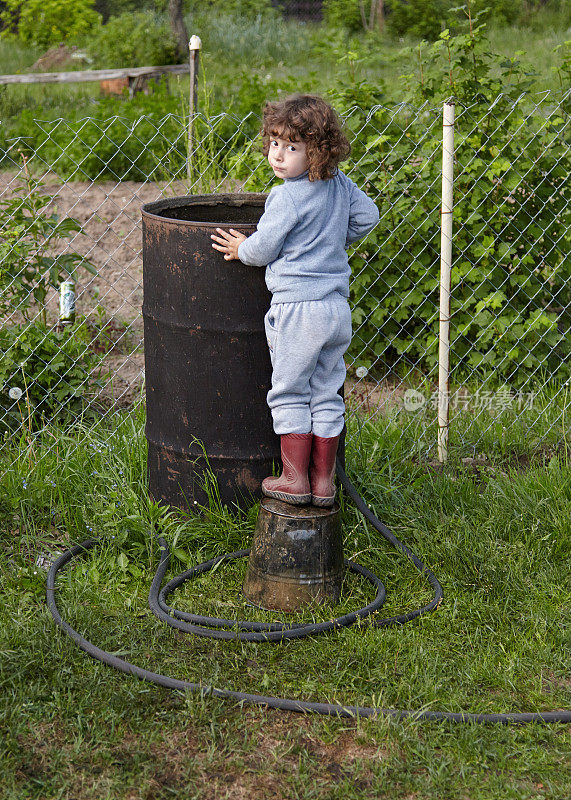一个孩子从软管里往大黑桶里注水的后视图