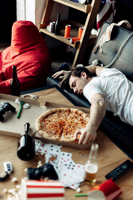 派对结束后，一个醉汉睡在沙发上，旁边是美味的披萨