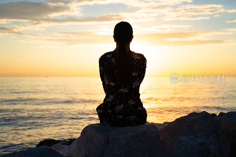 成年妇女坐在海滩上看日落的剪影