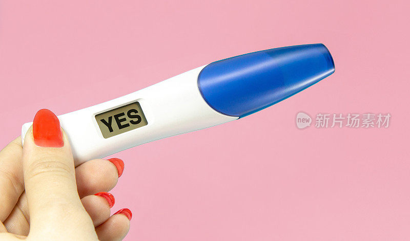 女人手握数码验孕棒孤立在粉红色上。妊娠测试呈阳性，回答是。