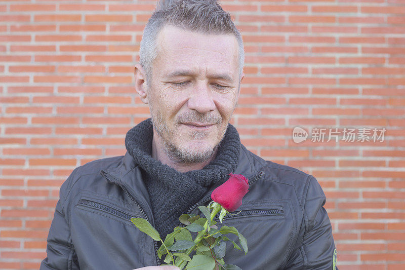 英俊的成年男子等待他的女朋友在室外与红玫瑰花在他的手作为礼物