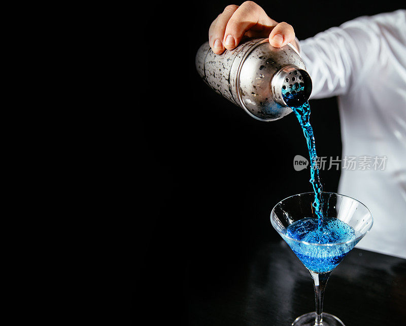 调酒师将蓝色鸡尾酒倒入马提尼酒杯
