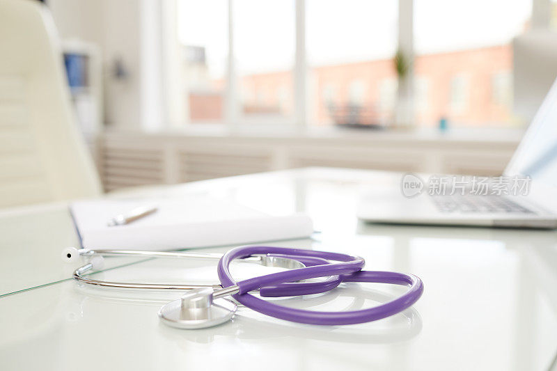 注重现代听诊器与紫色橡胶管放置在医生的桌子上，在充满光的办公室