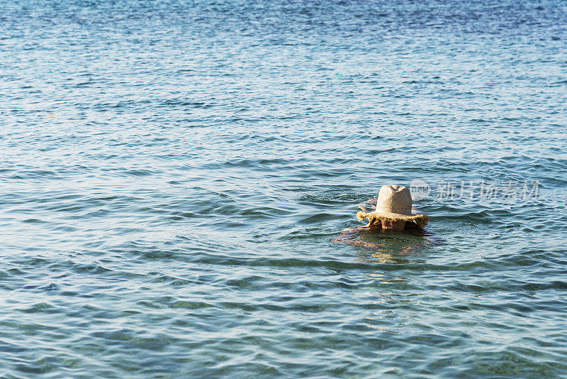 戴着柳条帽的女子在希腊海上进行蛙泳