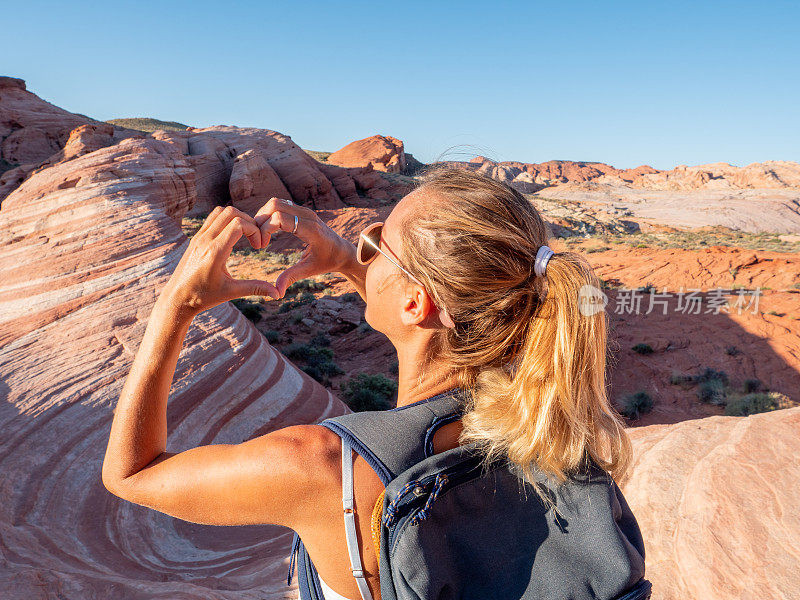一个徒步旅行的女人凝视着红色的砂岩，并在风景上制造爱心