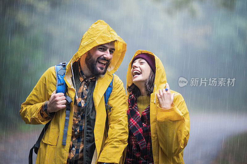 幸福的夫妇穿着雨衣，一边在森林里的雨中行走一边聊天。