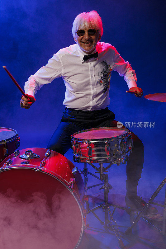 音乐家鼓手活跃的高级英俊男子打架子鼓。蓝色背景，光线和烟雾特效。