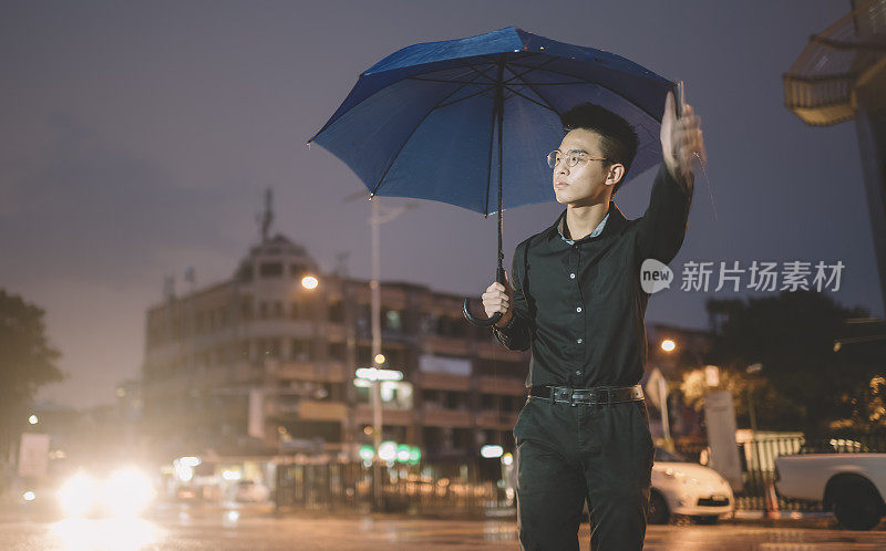 一个十几岁的亚洲华人男孩撑着伞在雨中行走在繁忙的街道上