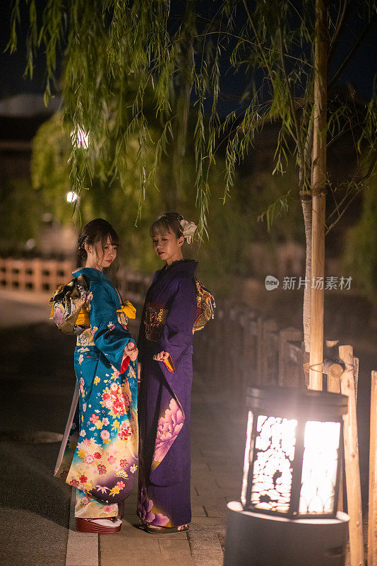 身着Furisode和服的年轻妇女在夜晚站在传统村庄的肖像