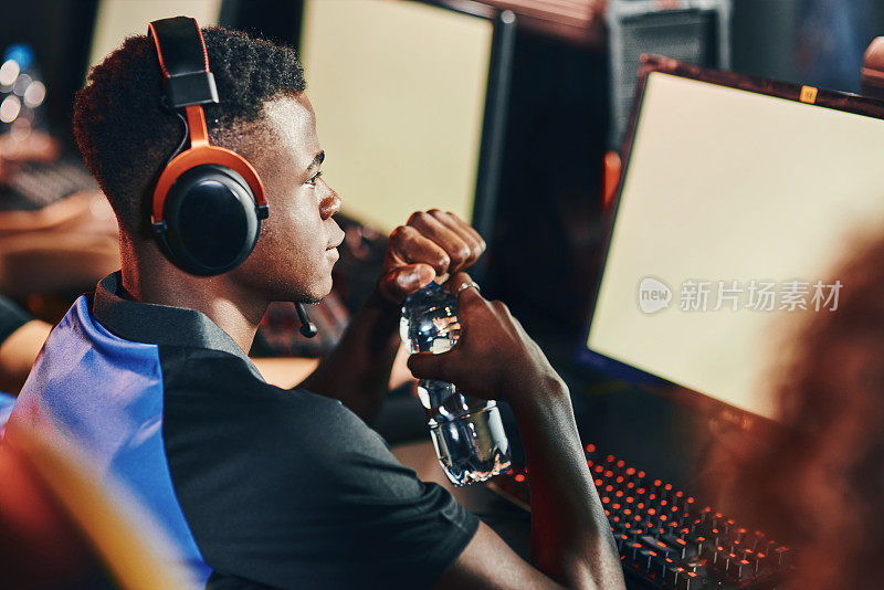 一位全神贯注的非洲职业电子竞技玩家戴着耳机玩在线视频游戏，看着电脑屏幕
