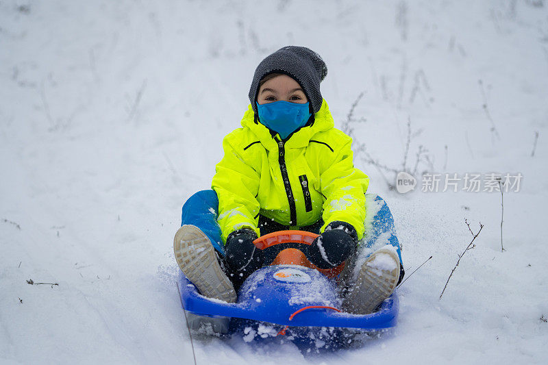 带着面罩的快乐微笑的男孩在雪地里和雪橇享受户外时光