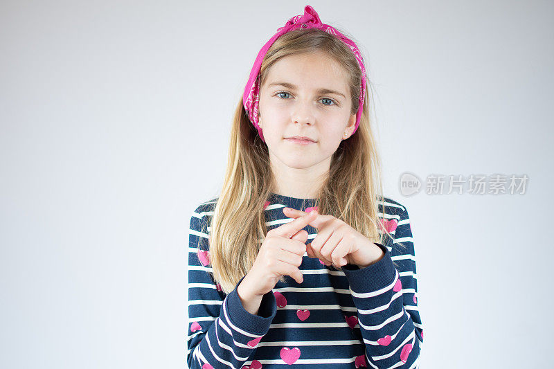 小女孩在白色的背景下用手指做着停止唱歌的动作。警告表情与否定和严肃的手势在脸上。