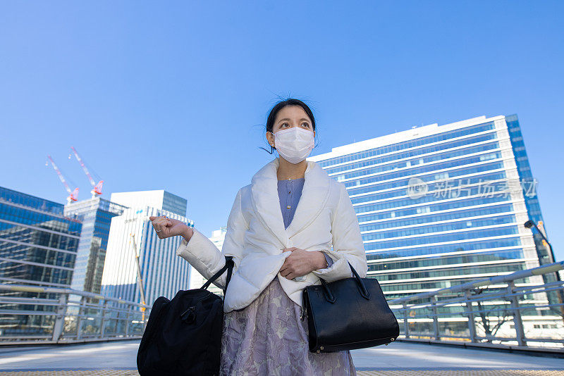 年轻的女商人戴着防护面罩走在城市的人行道上