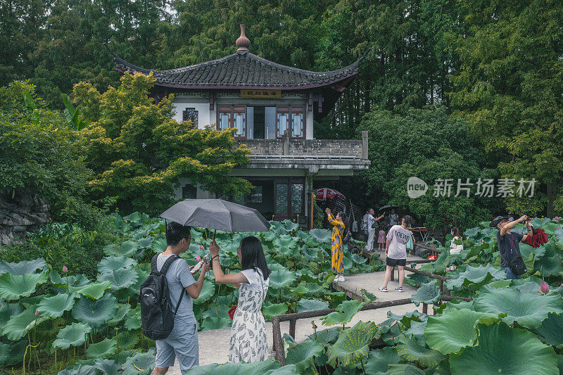 游客在西湖边一座中国传统民居前的一座桥上拍照