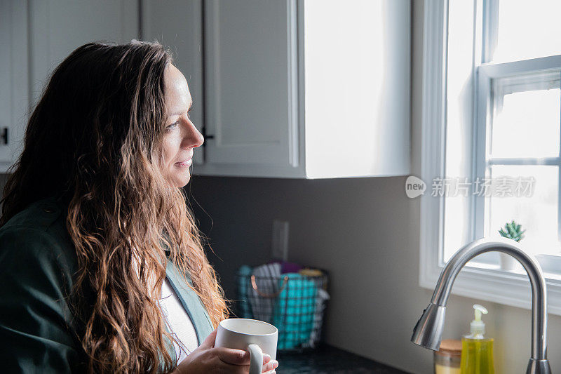 中年妇女喝着咖啡凝视着厨房的窗外