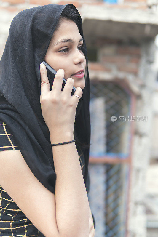 一名印度年轻女子用黑色的dupata盖住她，还在打手机，
