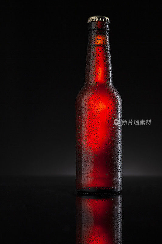 冰镇的棕色啤酒瓶覆盖着冰和水滴-凝结。用于饮料饮料产品设计模型的毛坯。站在黑色背景的黑色桌子上。