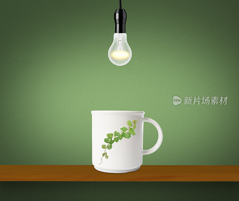 在架子上画有绿叶图案的马克杯上方挂了一个发光的灯泡。