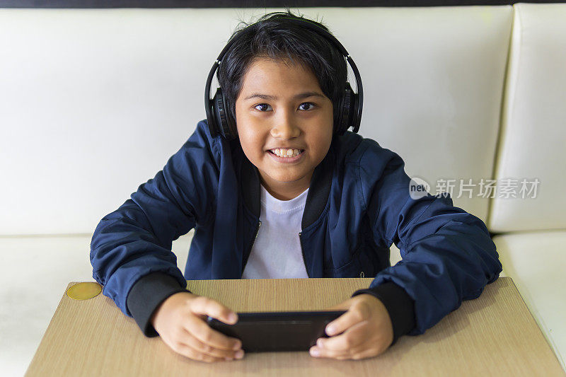小男孩戴着耳机用智能手机玩游戏