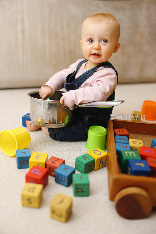 可爱的1岁小女孩开心地玩着锅鼓，周围是五颜六色的玩具和积木