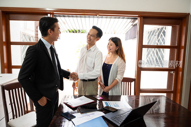亚洲夫妇在客厅成功签署房地产投资协议后与房地产经纪人握手。