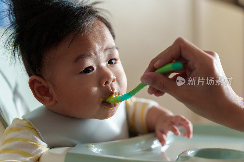 坐在高椅子上的亚洲小男孩正在被妈妈喂食。