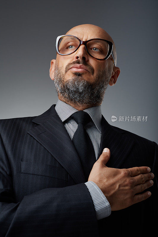 摄影工作室肖像一个中年自信和成功的商人与有趣的眼镜在一个黑暗的背景摆姿势