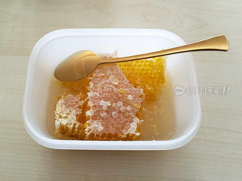 用金色勺子装在塑料盒里的蜂蜜