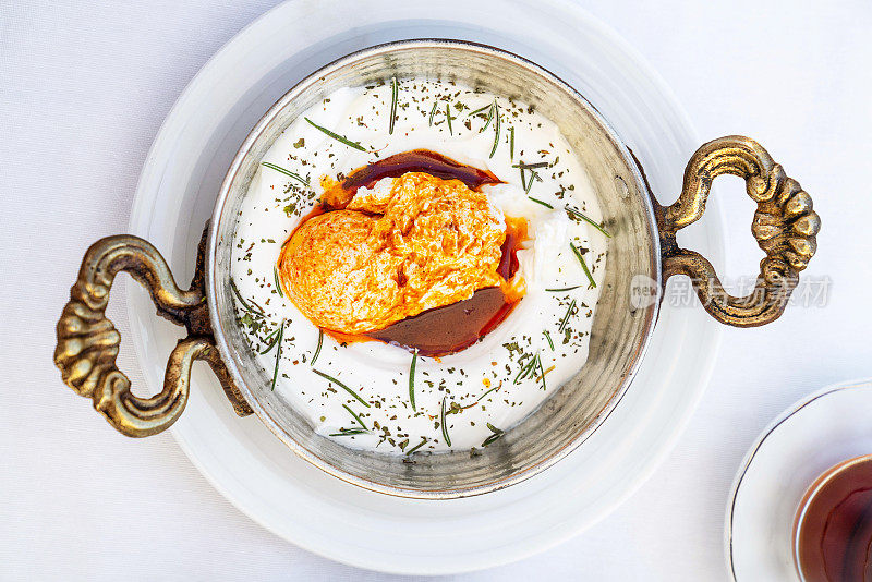 土耳其鸡蛋芫荽叶在白色的碗。土耳其菜系的概念。荷包蛋配酸奶和辣黄油酱。