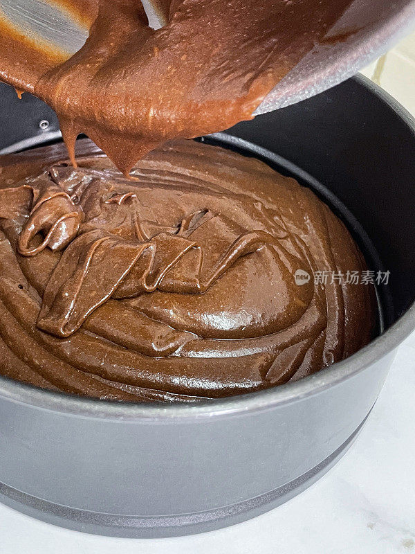 自制的维多利亚巧克力海绵蛋糕面糊，将黄油、糖、面粉和可可混合，从塑料搅拌碗中倒入内衬防油羊皮纸的不粘锅，大理石效果的厨房柜台