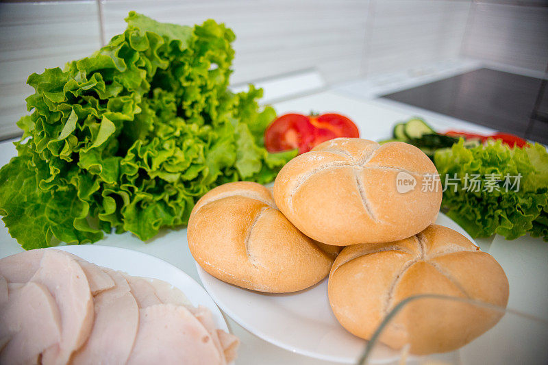 烹饪食品配料。意大利腊肠片，生菜沙拉，奶酪，黄油，面包，小面包，黄瓜，三明治和西红柿。俯视图