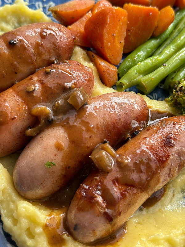 全帧图像的盘子传统的英国香肠和土豆泥，土豆泥顶部有两个猪肉香肠，绿色的西兰花，橙色的胡萝卜，覆盖在洋葱肉汁，丰盛的安慰食物，高处的视野