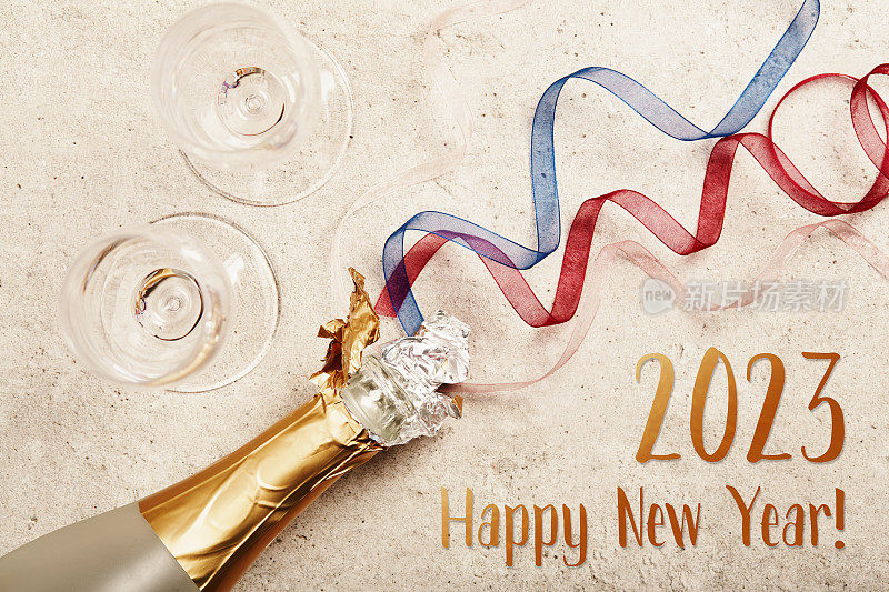 打开一瓶起泡酒或香槟和两个玻璃杯在水泥灰色表面，平放与2023年新年快乐的文字