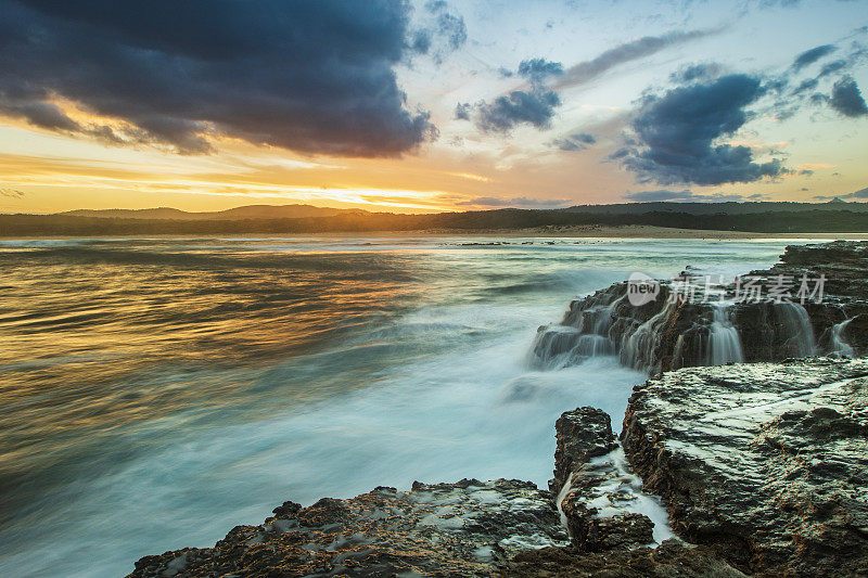 海浪和岩石的漫长探索与海洋上戏剧性的金色日落