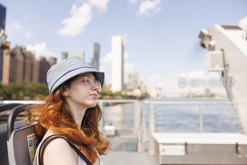 在一个阳光明媚的夏日，一位深思熟虑的年轻女子正在纽约市东河上乘坐渡轮。