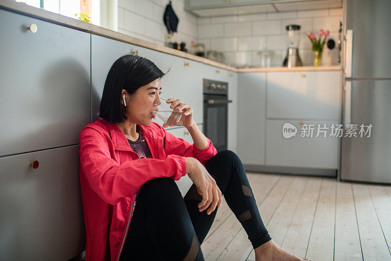 年轻的成年女性在锻炼后在厨房喝着一杯水