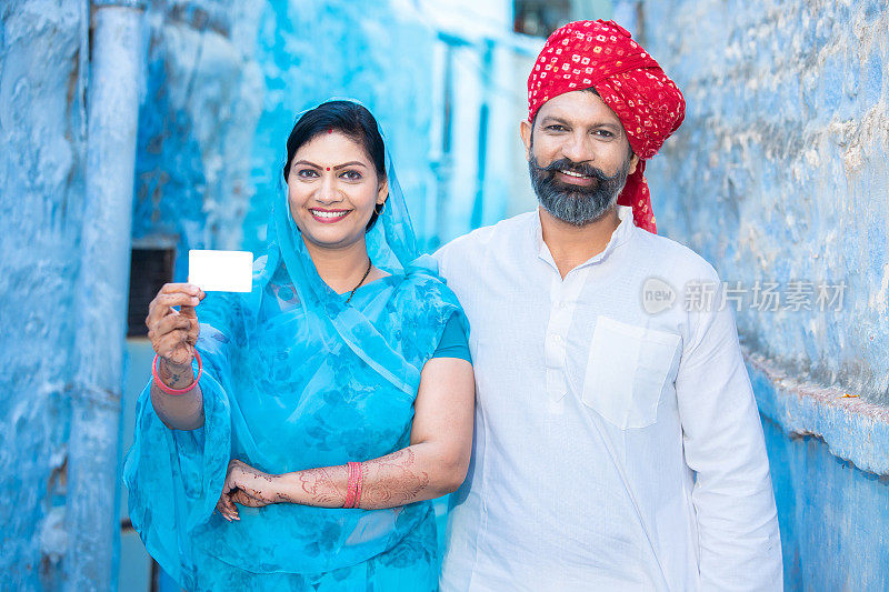 传统的印度夫妇展示空白的信用卡模型，快乐的拉贾斯坦夫妇穿着民族服装，拿着空的商务卡或电子卡付款。