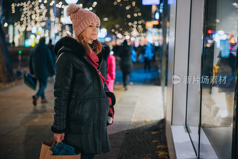 女人在冬季购物季，晚上看着商店橱窗