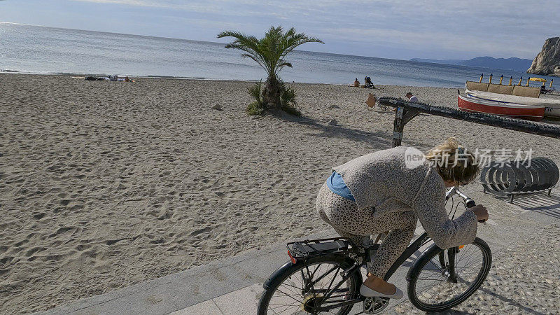年轻女子沿着海滩骑自行车