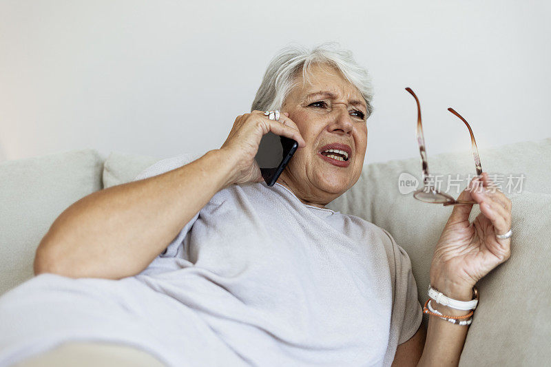 一位年长的女士在打电话。一位年长的女士在打电话。老年妇女坐在家里的沙发上打电话。
