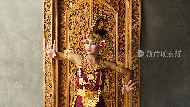 巴厘女孩穿着巴厘传统服饰，用王冠、珠宝和金饰饰品装点门面，以巴厘图案为背景