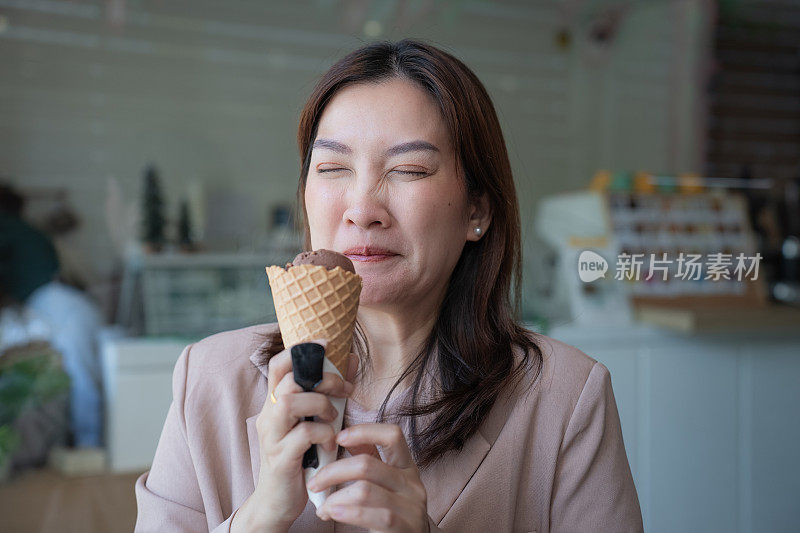 一位亚洲女商人下班后在一家咖啡馆吃冷冰淇淋当甜点，脸上露出因牙痛而焦虑的表情。