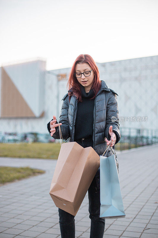 年轻的女人拎着购物袋，她站在街上打开袋子