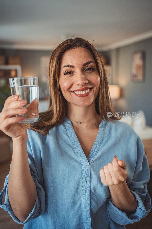 一个微笑的年轻美女的画像，手里拿着一杯新鲜干净的饮用水。健康生活方式和液体摄入的概念