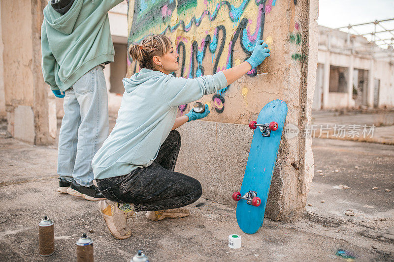 两位年轻的艺术家在一座废弃建筑的墙上涂鸦，共同创作了一件艺术作品